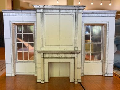 A white model of a decorative wall that has a fire place, molding, and two inset windows.