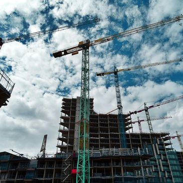 Multiple construction cranes towering over a building under construction on a partly cloudy day.