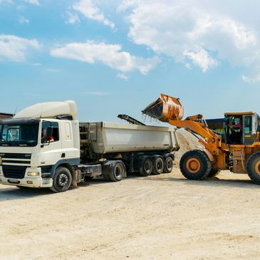 Yellow loader filling a white dump truck with gravel on a construction site.