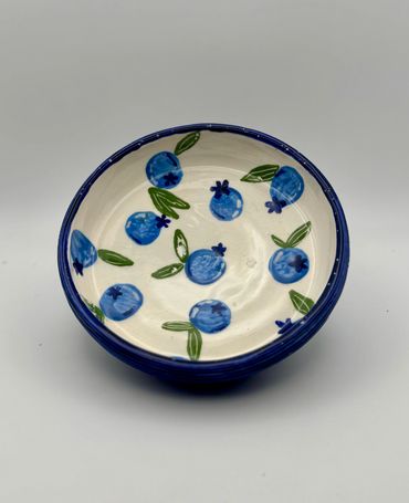 Ceramic bowl decorated with blue berries and green leaves.