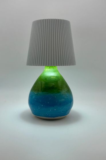 Table lamp with a blue-green glass base and white pleated shade.
