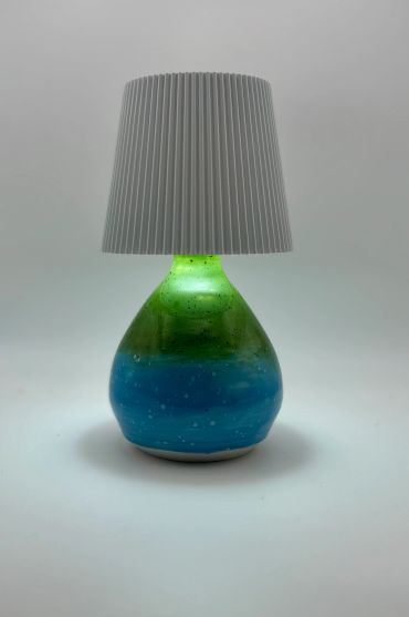 Table lamp with a blue-green glass base and white pleated shade.