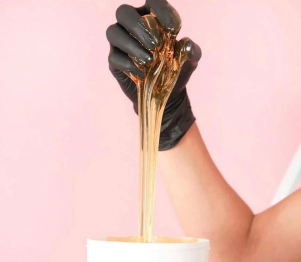 Hand in black glove stretching golden wax from a container.