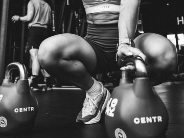 Person squatting in gym holding kettlebells.