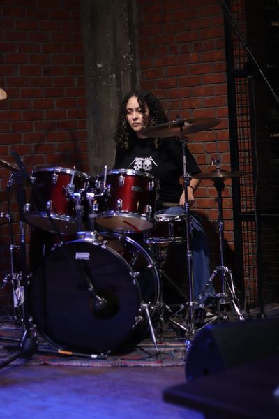 Person playing red drum set in a dark room.
