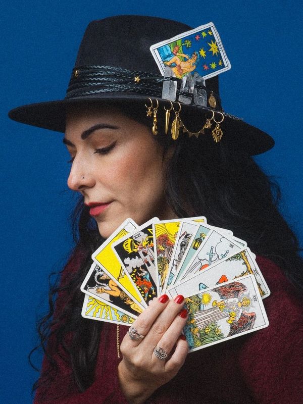 Woman holding tarot cards, wearing a decorated black hat.