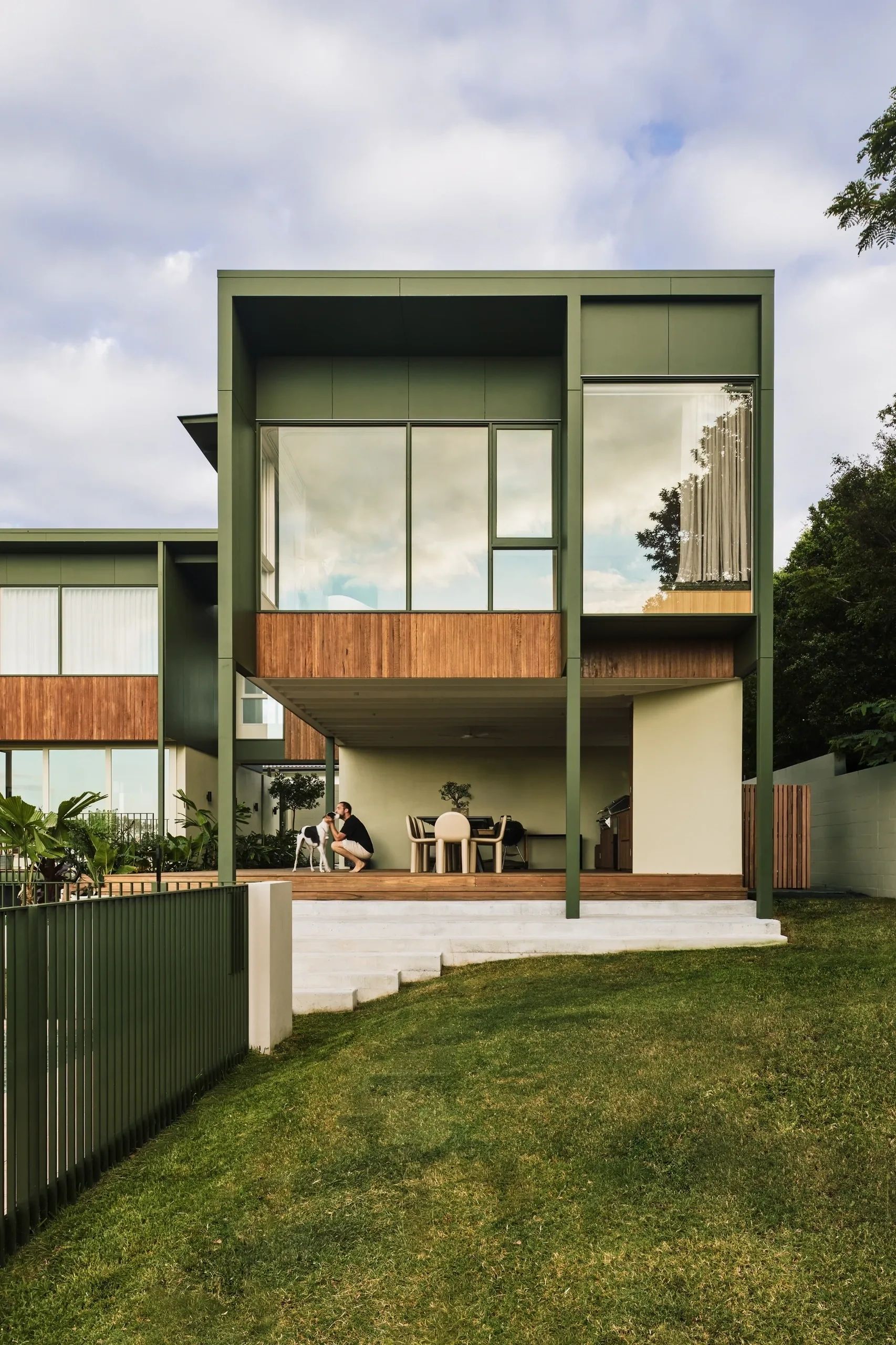 Modern house with green and wood exterior and a person playing with a dog.