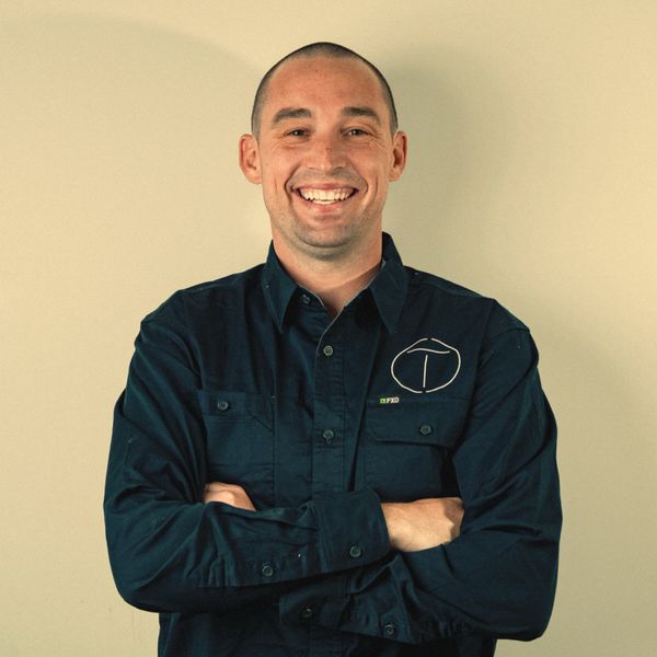 Smiling man in a dark button-up shirt with folded arms.