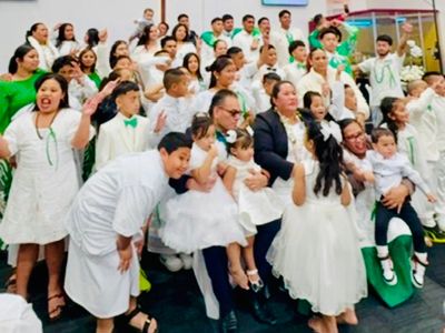 Large group dressed in white and green, joyfully posing indoors.