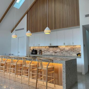 Modern kitchen with wooden stools and pendant lights.