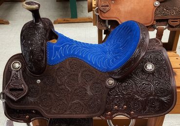 Intricately tooled leather saddle with vibrant blue seat.