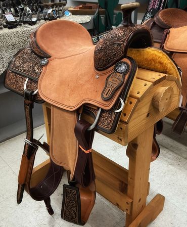 Close-up of a detailed leather horse saddle on a wooden stand.