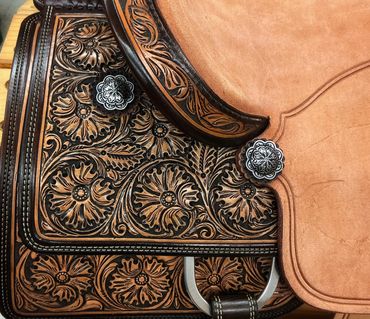 Intricately tooled leather saddle with floral patterns and decorative metal conchos.