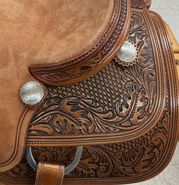 Close-up of detailed leather western saddle with engraved floral patterns.