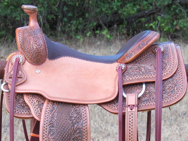 Intricately tooled leather Western saddle hanging on a rusty fence.