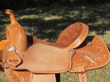 Intricately tooled leather saddle hanging on a fence.