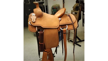 Light brown leather saddle on a stand indoors.
