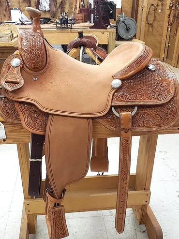 Detailed leather horse saddle on a wooden stand.