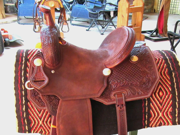 A detailed leather horse saddle on a patterned blanket.