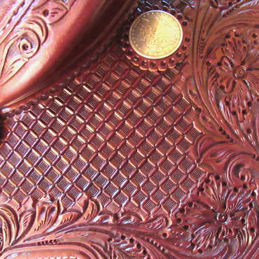 Close-up of intricately tooled brown leather with a coin.