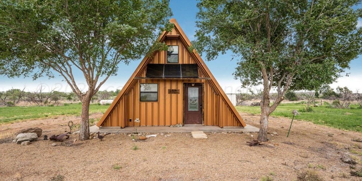 A triangular A-frame cabin with solar panels between two trees.