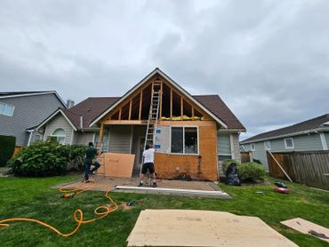 Two workers renovating the exterior of a house under a cloudy sky.