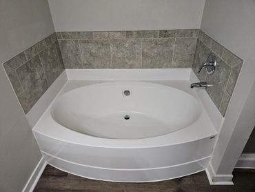 A clean white corner bathtub with tiled backsplash in a modern bathroom.