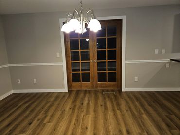 Empty room with wooden floor and glass-paneled double doors under ceiling light.