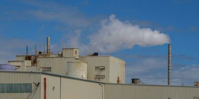 Factory with smokestack emitting white smoke under a blue sky.