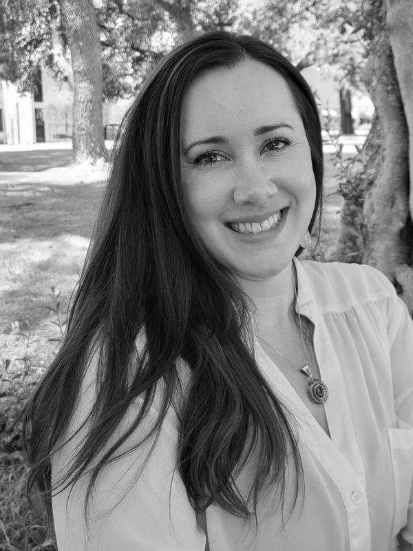 Smiling woman with long hair in a white blouse outdoors.