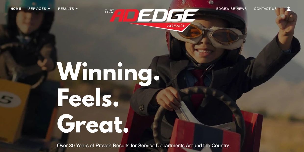 Child in aviator goggles celebrating while driving a toy car.