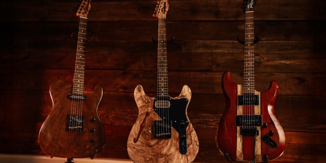 Three electric guitars on stands against a wooden wall.