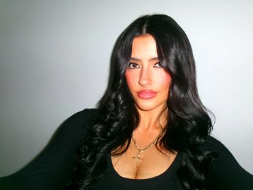 Close-up portrait of a woman with long black hair and a gold necklace.