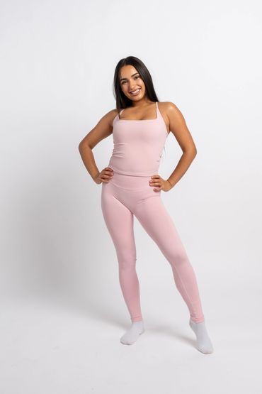 A smiling woman in pink activewear poses against a white background.