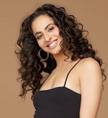 Smiling woman with curly hair wearing a black top and hoop earrings.