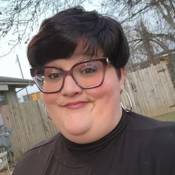 Woman with short dark hair and large glasses smiling outdoors.