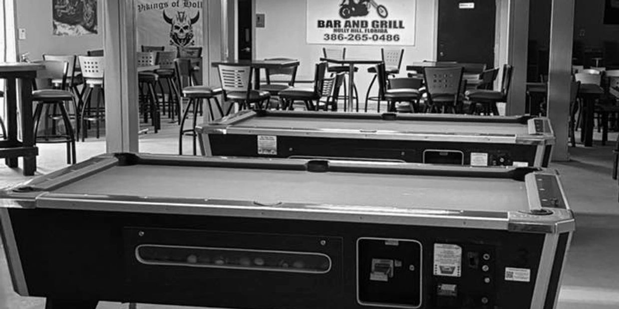 Pool tables under Bud Light lights in a bar with seating area.