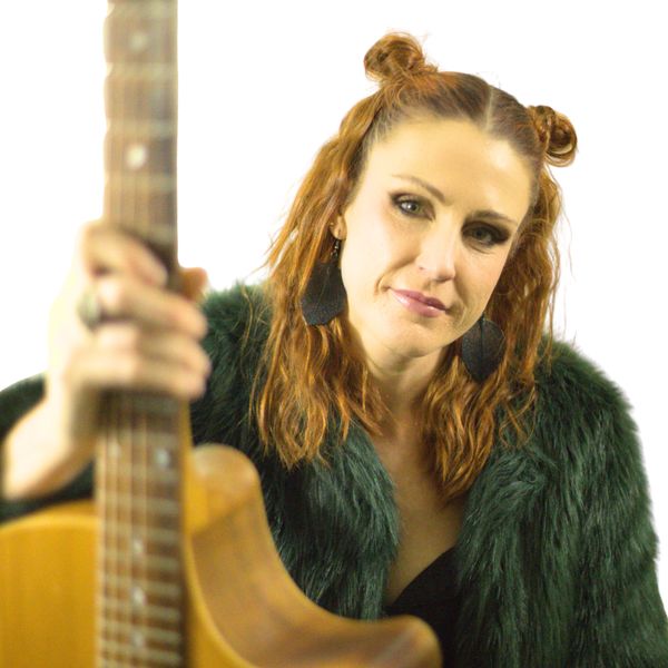 Woman holding a guitar, looking at the camera.