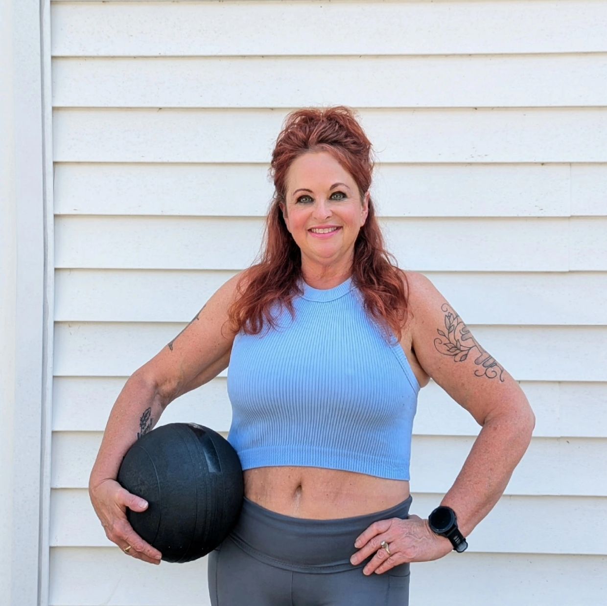 Smiling woman in workout attire holding a black medicine ball.