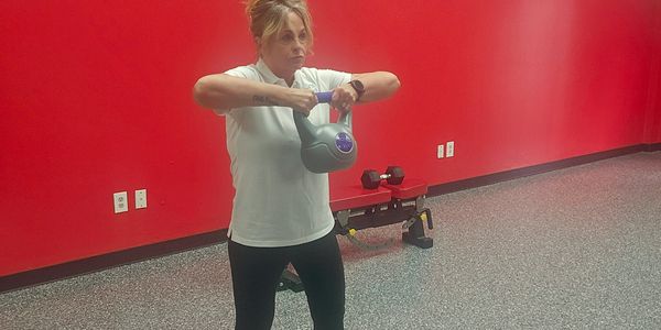 Woman exercising with a kettlebell in a gym with red walls.