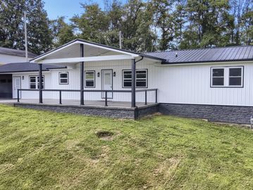 Modern white house with black roof and porch in a green yard.
