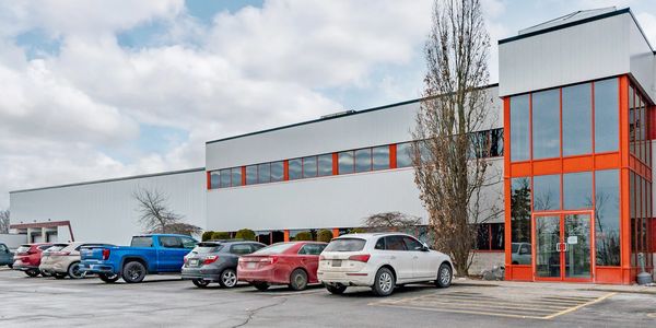 Modern industrial building with parked cars under a cloudy sky.