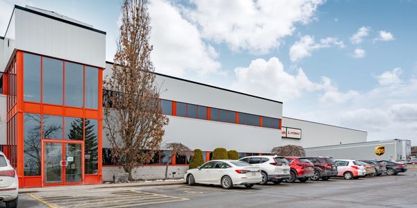Modern industrial building with a row of parked cars and a UPS truck in front.