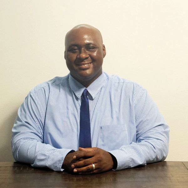 Man in checkered shirt and tie smiling at the camera.
