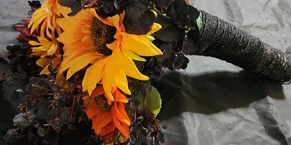 A bouquet featuring bright sunflowers and dark foliage on a black surface.