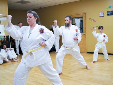 A family practicing a kata together in martial arts class, on a wood floor. Asheville Self Defense.