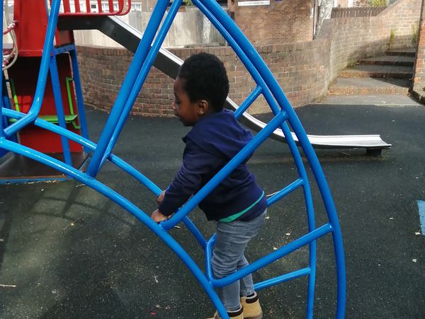 Cute African American little kid boy having fun while playing on the playground in the daytime 