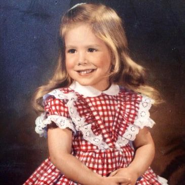 Young girl in a red plaid dress smiling.