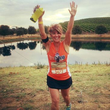 Runner celebrating with arms raised near a lake.