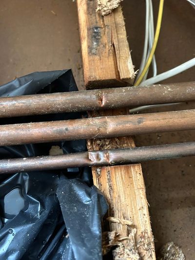 Three copper pipes with dents placed on wood.